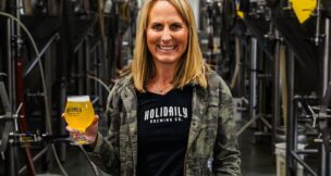 Blonde woman holding a beer in Holiday Brewing Co. brew room.