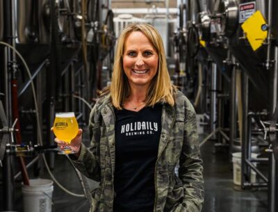 Blonde woman holding a beer in Holiday Brewing Co. brew room.