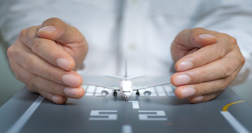 Airplane model on the runway and surrounded by hands. Concept of aviation safety, preventive action, security, and insurance.