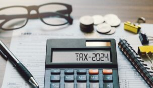 Word Tax 2024 on the calculator. Business and tax concept.Calculator, coins, book, form, and pen on table.Tax deduction planning.Financial research, government taxes, and calculation tax return