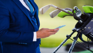 Man wearing a blue suit doing business on the golf course while on his phone, next to his golf bag.