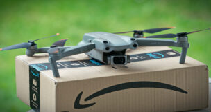 Selective focus on drone delivering parcel with amazon logo on cardboard. Milan, Italy - May 2021